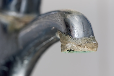 Close-up of limescale build-up. Selective focus on hard water deposit on old tap spout. Chrome kitchen or bathroom faucet with crusty calcium carbonate needing descaler.