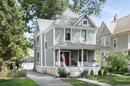 A beautifully renovated Victorian home with a grey and white siding, a covered front porch and a driveway leading to the backyard.
