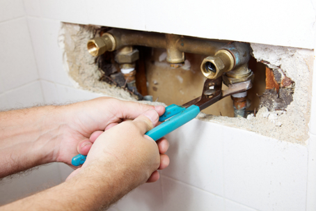 worker fixing a leaking pipe in the wall